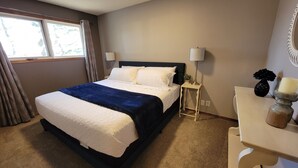 A neatly made bed with a dark headboard, a bedside table with a lamp, and a small vase with flowers. - Lovely Three Bedroom Farmhouse between Lethbridge and Coaldale (Coaldale)