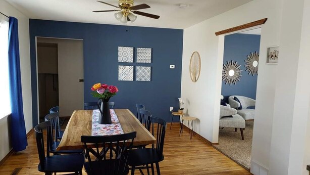 A dining area with a wooden table, black chairs, a ceiling fan, and a vase of flowers. - Lovely Three Bedroom Farmhouse between Lethbridge and Coaldale (Coaldale)