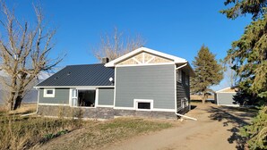 A two-story house with a garage, a stone foundation, and a sloped roof. - Lovely Three Bedroom Farmhouse between Lethbridge and Coaldale (Coaldale)