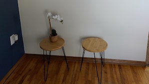 A room with a wooden floor, two round tables with black legs, a wall-mounted circular decorative piece, and a small potted plant with white flowers. - Lovely Three Bedroom Farmhouse between Lethbridge and Coaldale (Coaldale)
