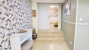 A hallway with patterned wallpaper, a bench, a potted plant, and a staircase leading to another room. - The Leneade - Mobo Apt. 6 at City Centre/Wuse 2 (Abuja)