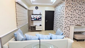 A modern living room with a sofa, a glass coffee table, and a TV mounted on the wall. There is a door and a patterned wall in the background. - The Leneade - Mobo Apt. 6 at City Centre/Wuse 2 (Abuja)