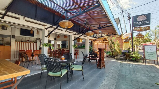Un espace extérieur aménagé pour les repas, avec des tables et des chaises, un coin salon abrité et une enseigne indiquant le nom de l’établissement : The Tunjung Boutique Resort.