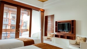 Une chambre d’hôtel avec deux lits, une télévision, un canapé et un balcon donnant sur des immeubles.