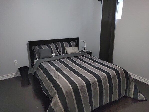 Une chambre à coucher avec un lit, une table de chevet, une lampe et une fenêtre.