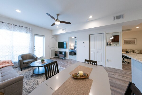 A modern living room with a dining area, a ceiling fan, and a TV. - Modern One Bedroom + Study private condo unit|2P (Katy)