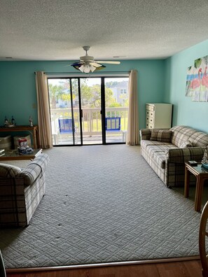A living room with a large carpet, two plaid sofas, a coffee table, and a ceiling fan. - Feel @ Home in Casita Cruz, Pool, 2miles beach, Laundry, King Bed & Free Parking (Myrtle Beach)