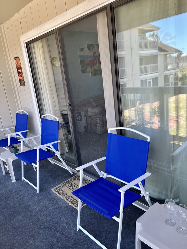 A balcony with blue and white chairs, a small table with wine glasses, and a view of a building with balconies.