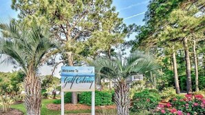 Une pancarte accueillant les visiteurs de Gulf Colony, avec en arrière-plan des palmiers et des arbustes en fleurs.