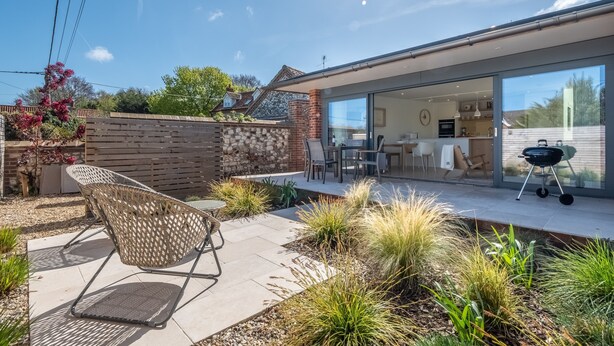 Una casa moderna con patio, mobiliario exterior y zona de barbacoa.