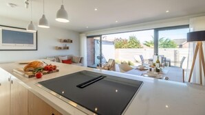 Una cocina moderna con una isla grande, iluminación colgante y vista a un comedor exterior.