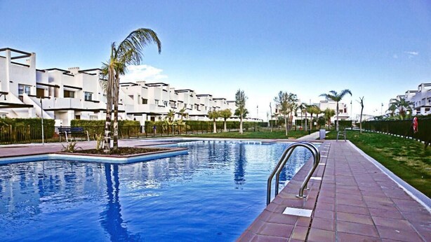 A swimming pool with a tiled walkway, surrounded by modern buildings and palm trees.