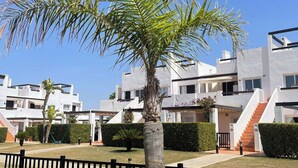 A modern residential building with a central staircase, surrounded by well-maintained lawns and palm trees.