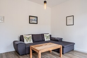 Ein modernes Wohnzimmer mit einem grauen Sofa, zwei Schmetterlingskissen, einem Holztisch und zwei gerahmten Bildern an der Wand.