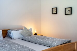 Ein ordentlich bezogenes Bett mit gemusterten Betttextilien, eine Nachttischlampe und zwei gerahmte Bilder an der Wand.