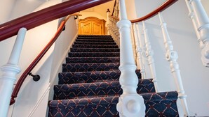Un escalier recouvert d’une moquette à motifs, avec des balustrades blanches et une main courante en bois.