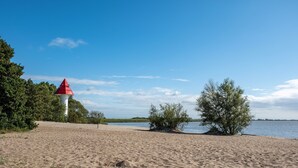 Une plage de sable avec un phare rouge, des arbres et une étendue d’eau calme.