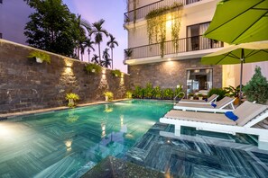A swimming pool with lounge chairs and umbrellas, surrounded by stone walls and plants. - Tomorrow Villa Hoi An (Da Nang)