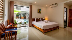 A hotel room with a bed, a dining area with a table and chairs, a window with curtains, and a view of an outdoor area. - Tomorrow Villa Hoi An (Da Nang)