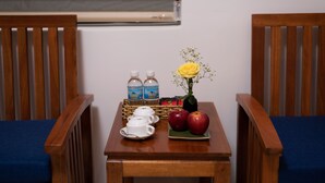 A wooden table with a blue cushion, two wooden chairs, a vase with a yellow flower, two apples, two bottles of water, and a basket of snacks. - Tomorrow Villa Hoi An (Da Nang)