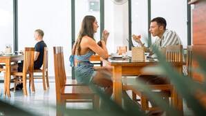 A modern dining area with wooden tables and chairs, large windows, and a fan. - Tomorrow Villa Hoi An (Da Nang)