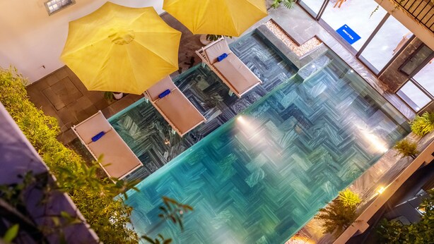 An indoor swimming pool with clear water, surrounded by yellow umbrellas and potted plants. - Tomorrow Villa Hoi An (Da Nang)