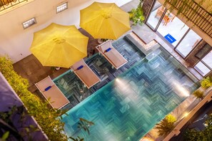 An indoor swimming pool with clear water, surrounded by yellow umbrellas and potted plants. - Tomorrow Villa Hoi An (Da Nang)