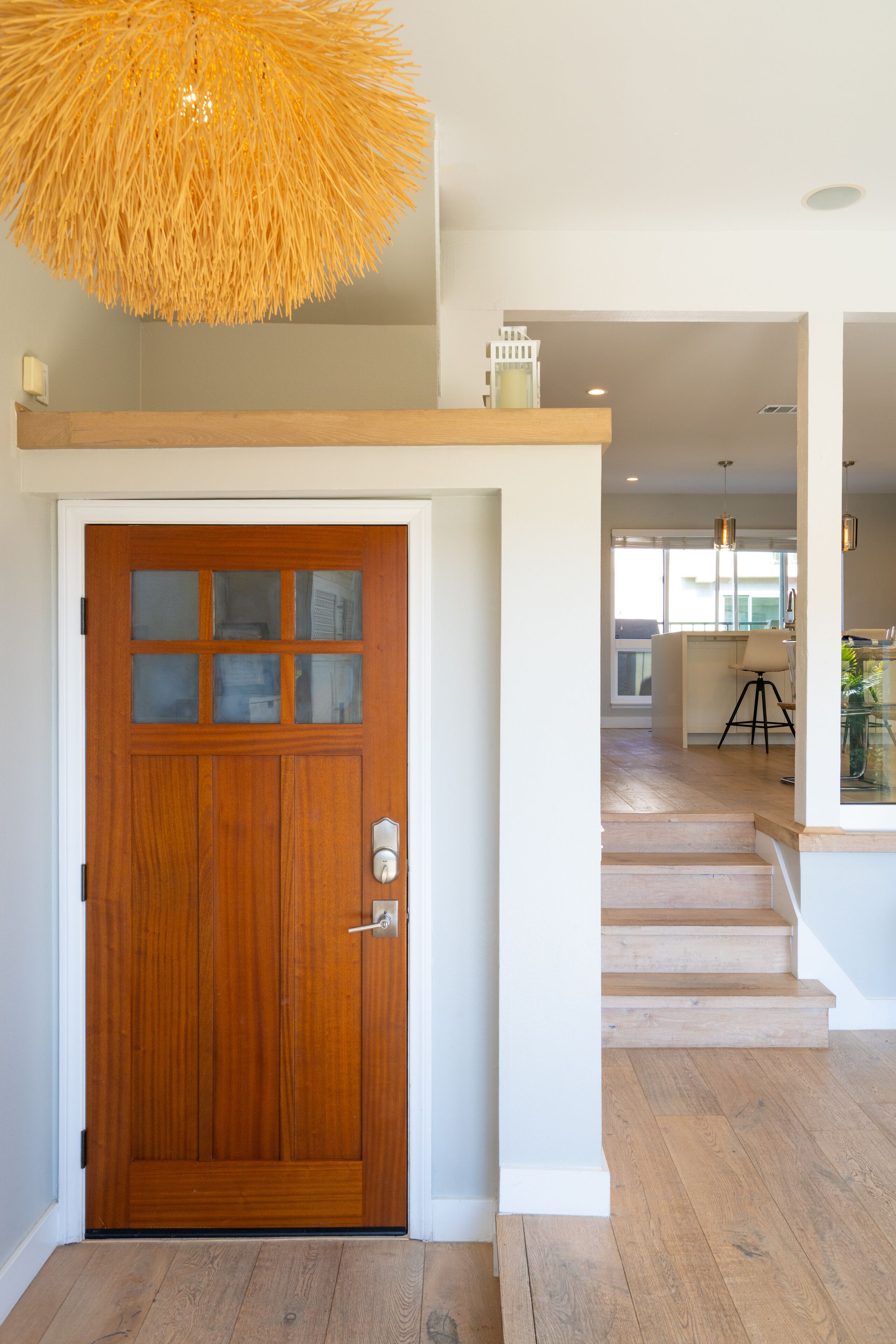 Une porte en bois avec un panneau de verre, un luminaire suspendu et un escalier menant à un étage supérieur.