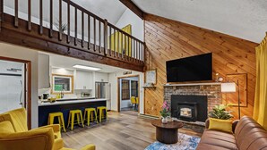 A spacious living area with a fireplace, yellow bar stools, a sofa, and a television mounted on the wall.