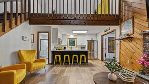 A modern kitchen with a central island, yellow bar stools, and wooden flooring.