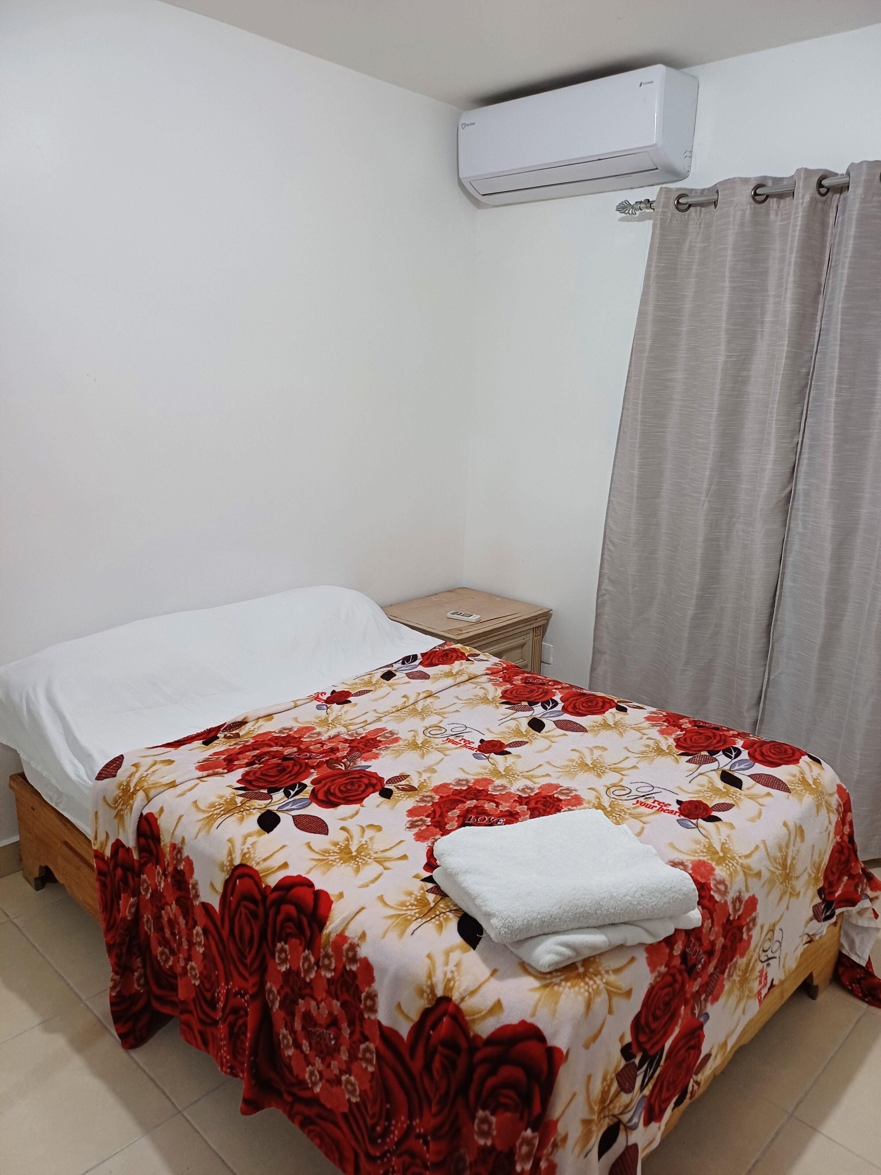 Un dormitorio con cama, mesita de noche, aire acondicionado y cortina.