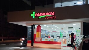 Una farmacia llamada 'Farmacia Patrizo' con una entrada bien iluminada y un coche estacionado frente a ella.