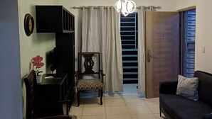 Una sala de estar con sofá, sillón, mesa, televisor, planta y una escalera que lleva a un balcón.