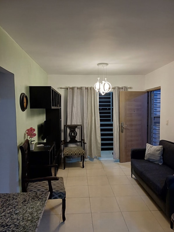 A living room with a sofa, a chair, a table, a TV, a plant, and a staircase leading to a balcony.
