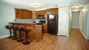 Una cocina con armarios de madera, un refrigerador negro, un microondas y una zona con taburetes de bar.