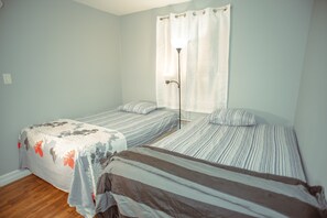 A room with two single beds, a window with a curtain, and a floor lamp. - Beautiful 3 Bedroom house - 15 Mins away from Brackley Beach (Milton Station)
