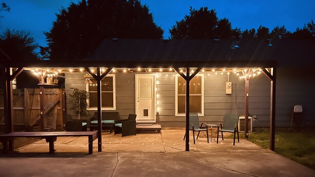 Een overdekt terras met lichtjes, zitplaatsen en een houten terras.