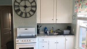 Una cucina con mobili bianchi, un fornello, un lavello e un grande orologio a parete.