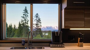 Cozinha moderna com vista para árvores e montanhas, cafeteira e porta-facas.