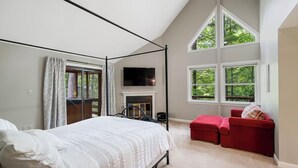 Une chambre à coucher avec un lit à baldaquin, une cheminée, une télévision et de grandes fenêtres.