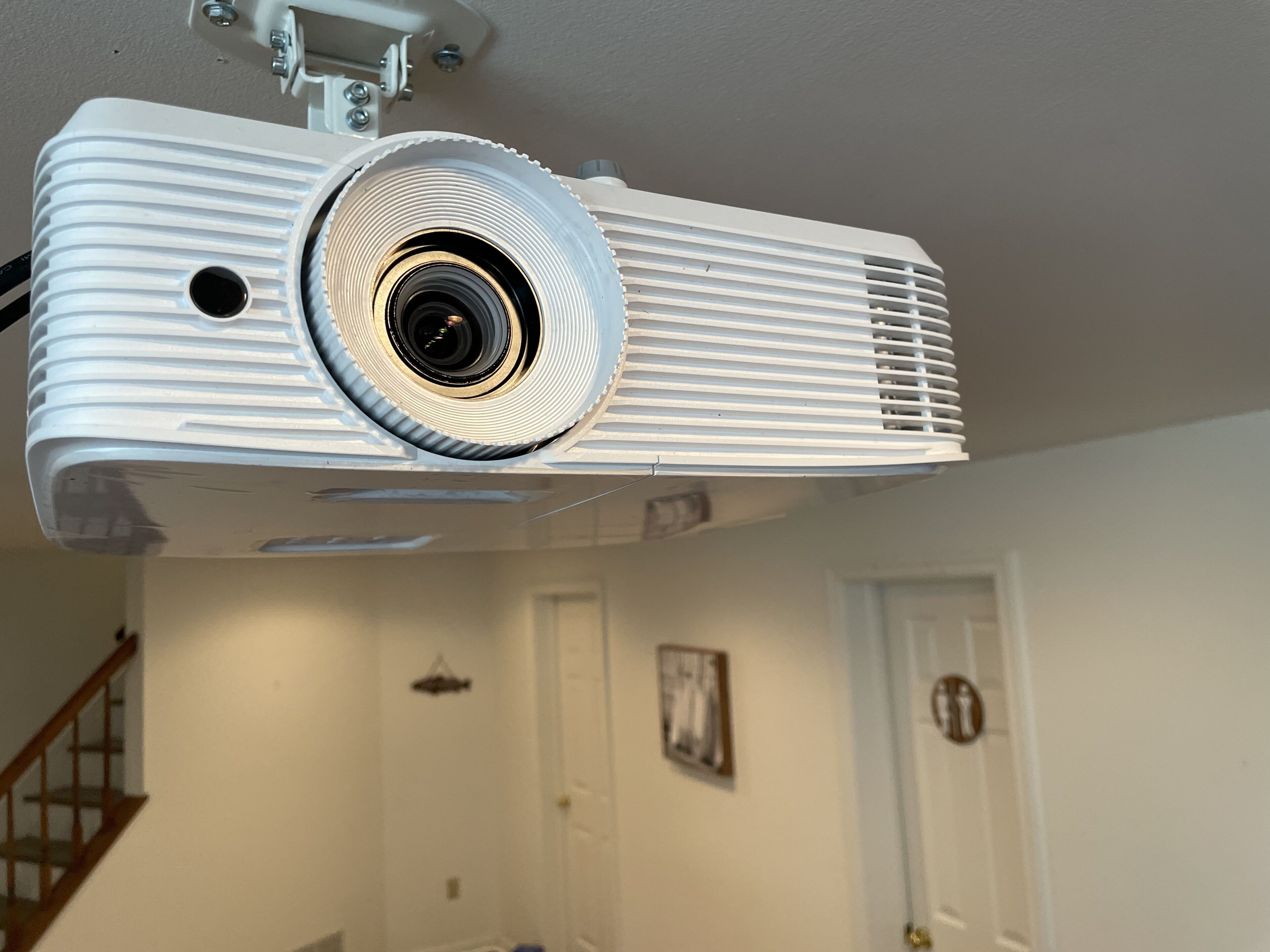 A white ceiling-mounted projector in a room with a staircase and a door.