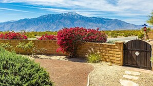 A gated entrance with a stop sign, a brick wall, and vibrant red bougainvillea bushes. - NEW: Pool, Spa, Tiki Bar, Mini Golf, Firepit, Desert Views (Desert Hot Springs)