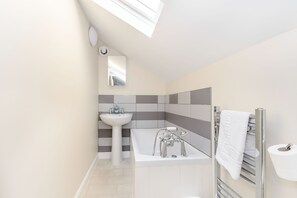 Un baño moderno con tragaluz, bañera, lavabo y perchero para toallas.