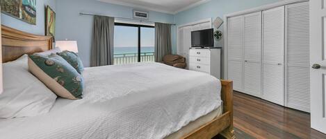 A bedroom with a bed, a ceiling fan, a TV, a closet, and a view of the ocean.