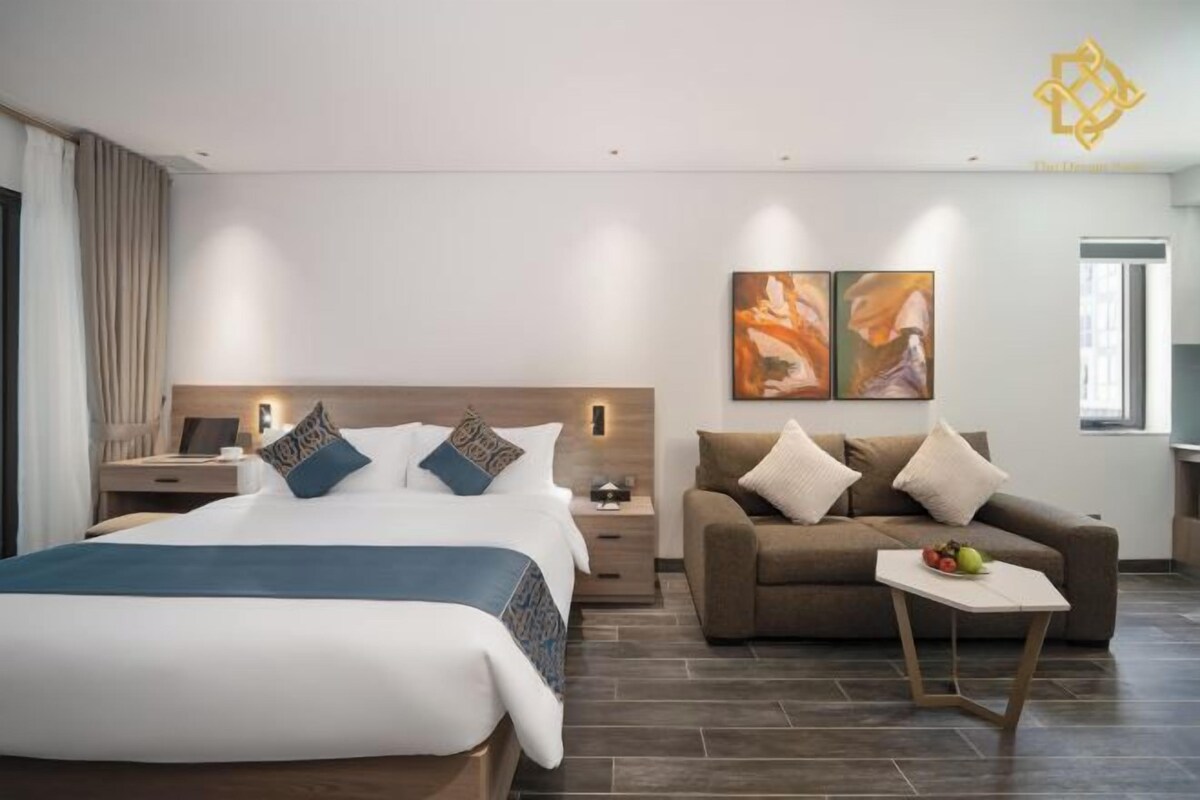 A modern hotel room with a large bed, a sofa, a small table with fruit, and abstract art on the wall.
