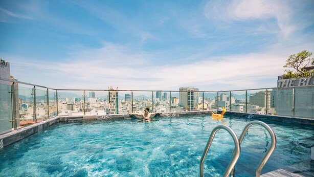 A rooftop infinity pool with a city skyline view, a glass railing, and a clear sky. - The Dream Suite (Da Nang)
