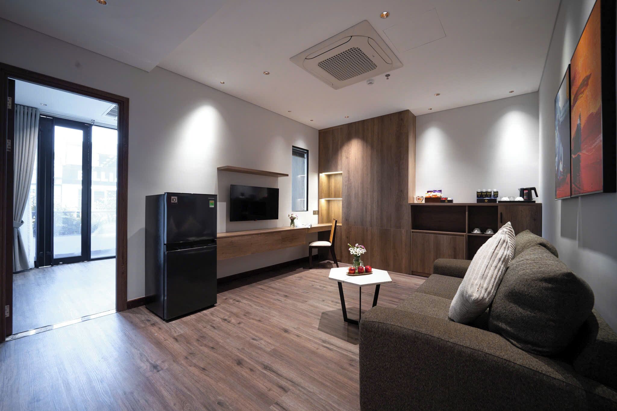 A modern hotel room with a flat-screen TV, a wooden cabinet, a sofa, and a small table with a vase.