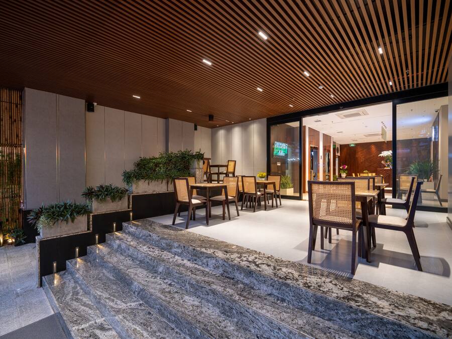 Un espacio interior moderno con techo de listones de madera, una escalera de mármol y varias mesas y sillas.