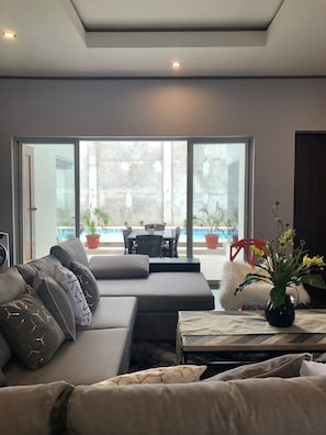 A modern living room with a sectional sofa, a coffee table, and a view of an outdoor patio with a pool and dining area.