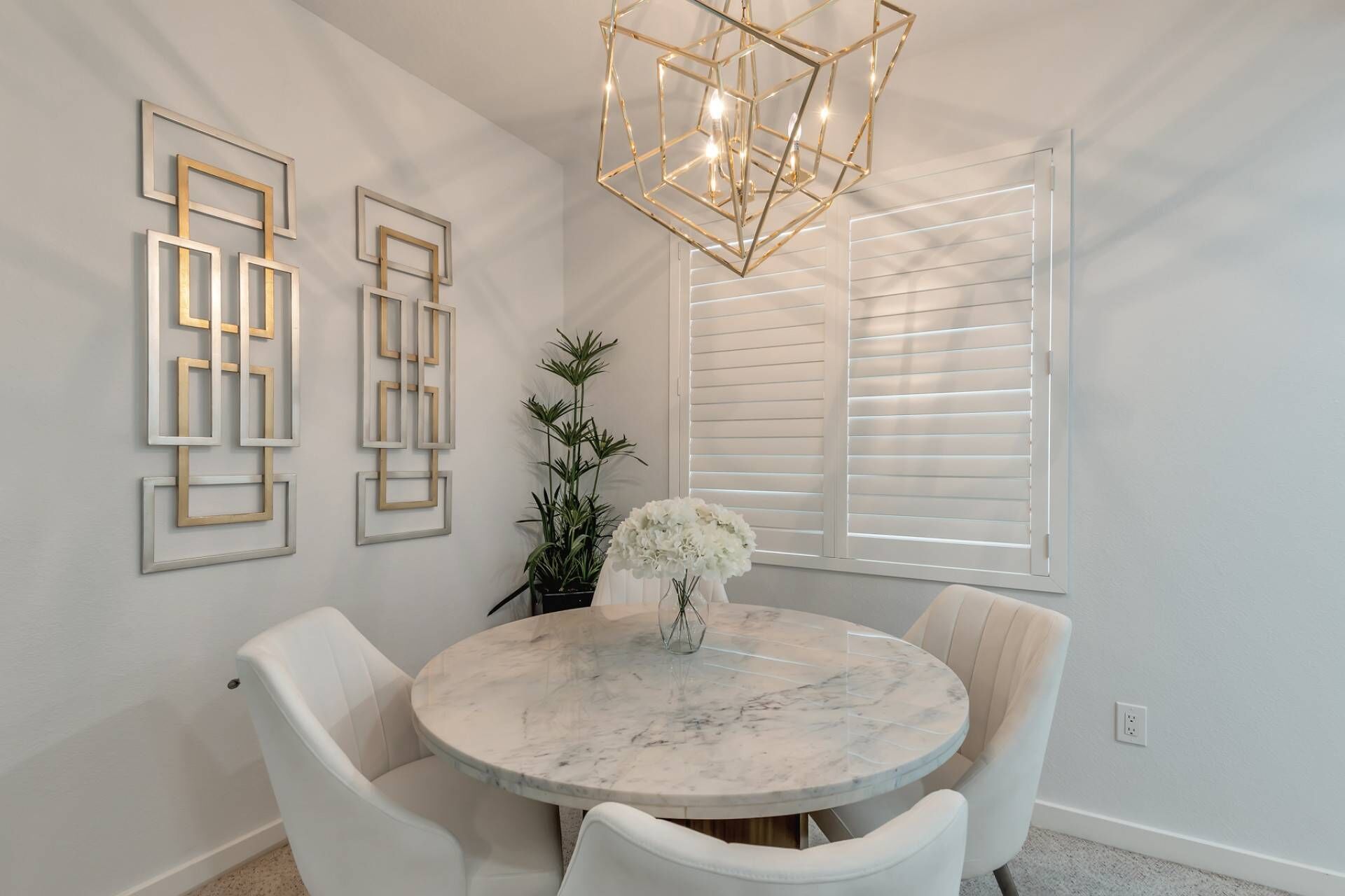 A dining area with a round marble table, white chairs, a chandelier, and framed wall art.